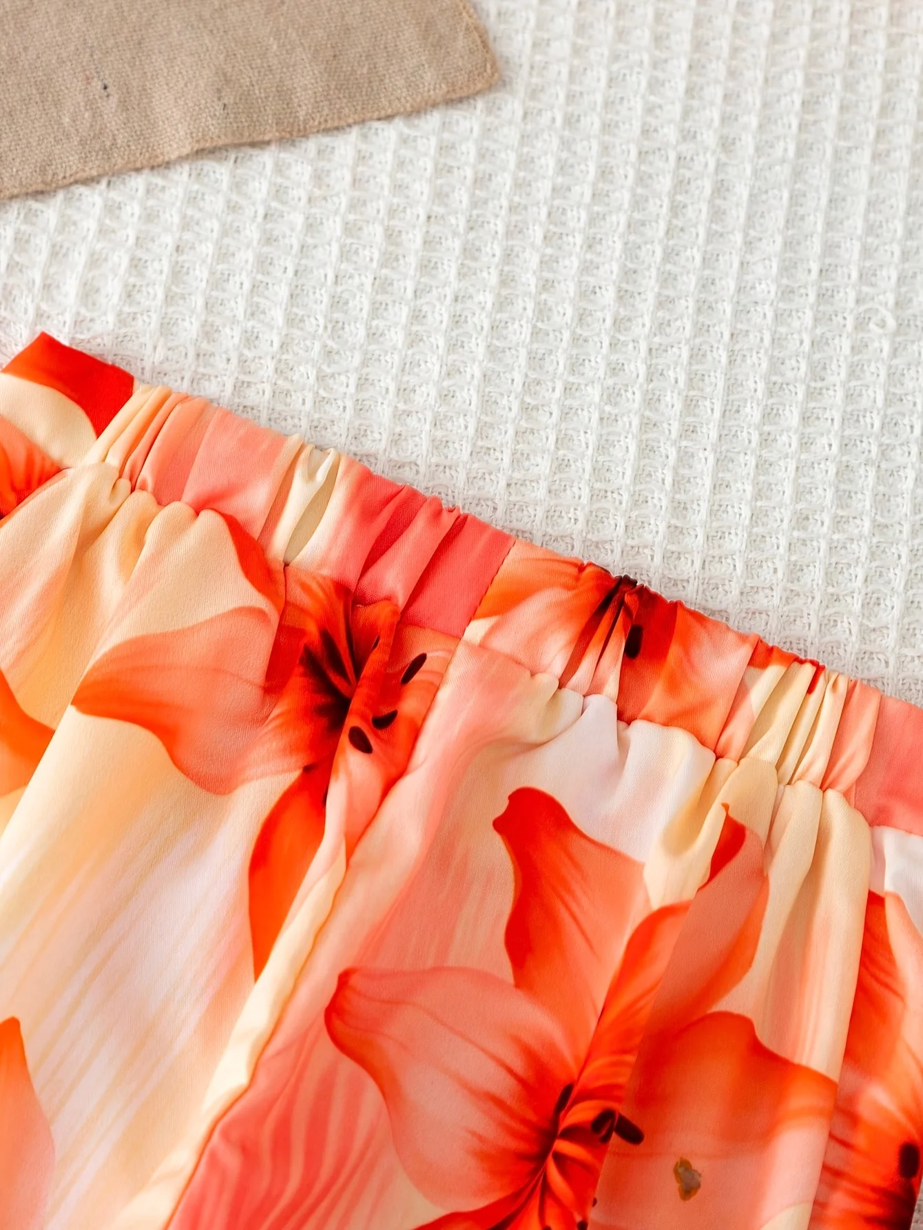 Conjunto de dos piezas estilo vacacional naranja para niñas: top corto sin mangas con cuello simulado, de color liso y textura acanalada, combinado con pantalón fluido con estampado de lirios.